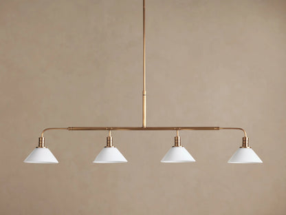 Theron Linear Chandelier with four milk glass cones on a horizontal brass bar, suspended against a warm brown wall.