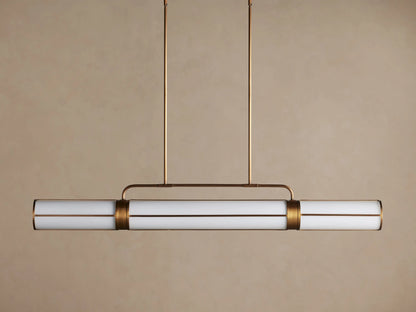 Remming Linear Chandelier with illuminated milk glass rods and burnished brass frame, hanging against a light brown wall.