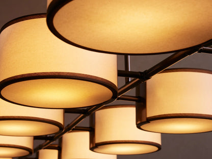 Nine cream-colored drum pendant lights in a row, with black trim and metal supports, against a beige background.