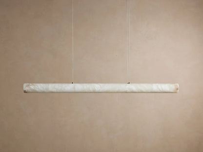 Halima Linear Chandelier with glowing alabaster stone, elongated horizontal bar, suspended by thin steel cables against a beige background.
