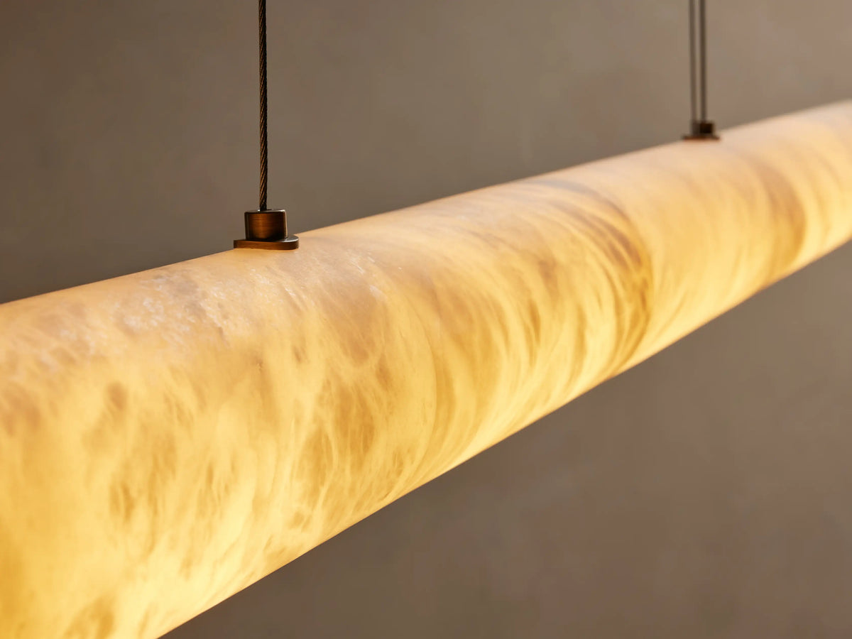 Halima Linear Chandelier with glowing elongated alabaster stone tube, suspended by a steel cable against a neutral background.