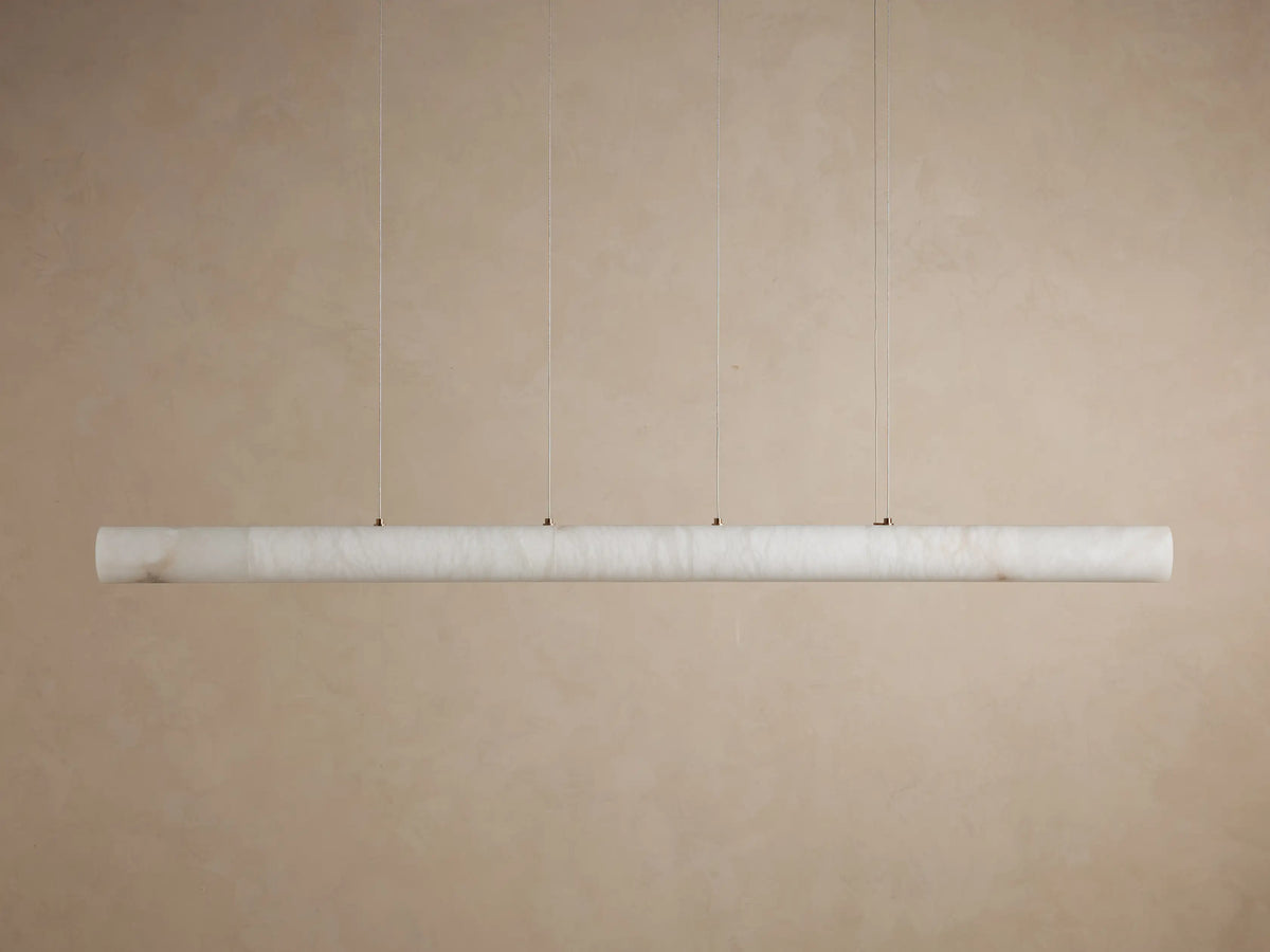 Halima Linear Chandelier with alabaster stone finish, suspended by steel cables, glowing warmly on a plain background.