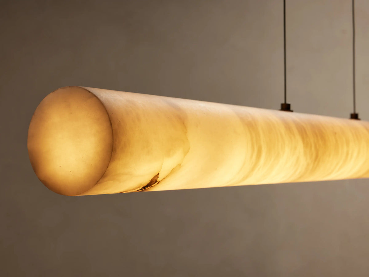 Halima Linear Chandelier made of alabaster stone, suspended by four steel cables, against a beige background.