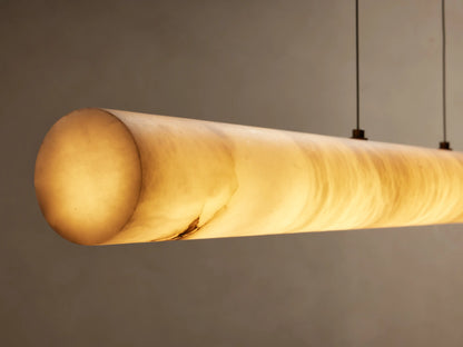 Halima Linear Chandelier made of alabaster stone, suspended by four steel cables, against a beige background.