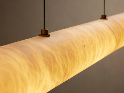 Halima Linear Chandelier made of Spanish alabaster stone with warm amber glow, suspended by steel cables against a neutral background.