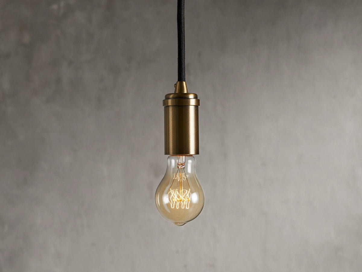 Ohlson Brass Swag Pendant with a brass-plated finish, hanging against a textured gray background.