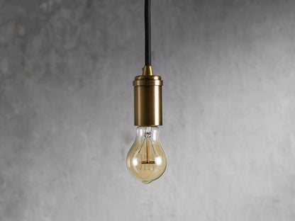 Ohlson Brass Swag Pendant with a brass-plated finish, hanging against a textured gray background.