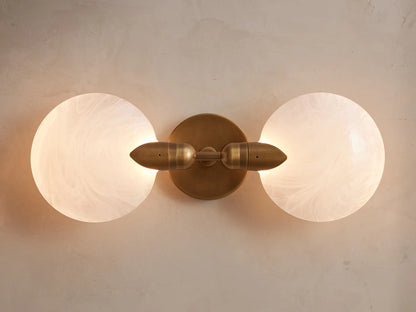 Lyla Double Sconce with hand-blown glass globes and brass plate, mounted vertically on a wall, with a soft glow.