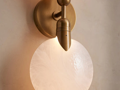 Lyla Double Sconce with two glowing hand-blown glass spheres mounted on a central brass steel backplate against a neutral wall.