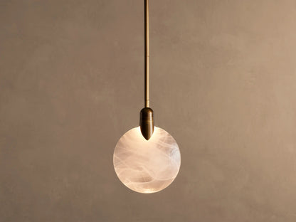 Lyla Single Pendant, a brass-plated fixture with a glowing, spherical hand-blown glass shade featuring white swirls.