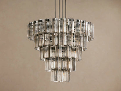 Delsie Round Chandelier, tiered with many illuminated clear fluted glass rods, suspended against a warm brown wall.