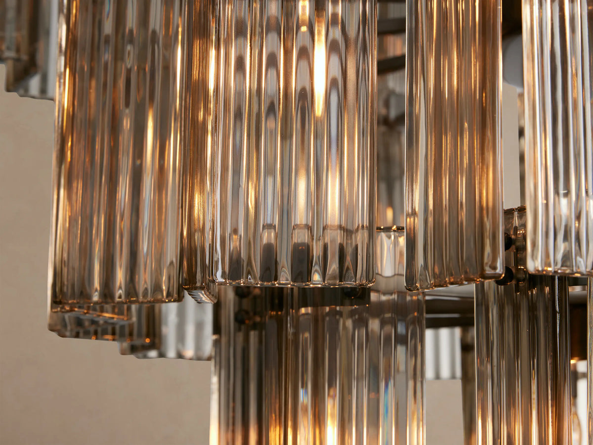 Delsie Round Chandelier, a tiered design with multiple vertical clear glass rods and dark metallic frames, against a beige wall.