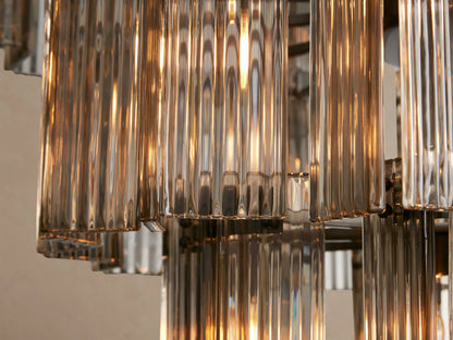 Delsie Round Chandelier, a tiered design with multiple vertical clear glass rods and dark metallic frames, against a beige wall.