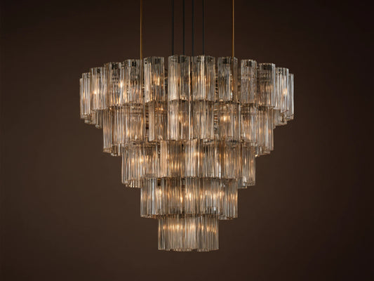 Delsie Round Chandelier, tiered with many illuminated clear fluted glass rods, suspended against a warm brown wall.