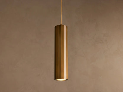 A cylindrical pendant light with a glossy brass finish hangs from the ceiling against a plain beige background.