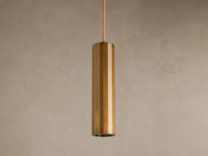 A cylindrical pendant light with a glossy brass finish hangs from the ceiling against a plain beige background.