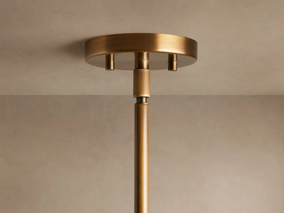A close-up of a modern pendant lamp with a brass finish and a frosted glass dome, set against a neutral wall.