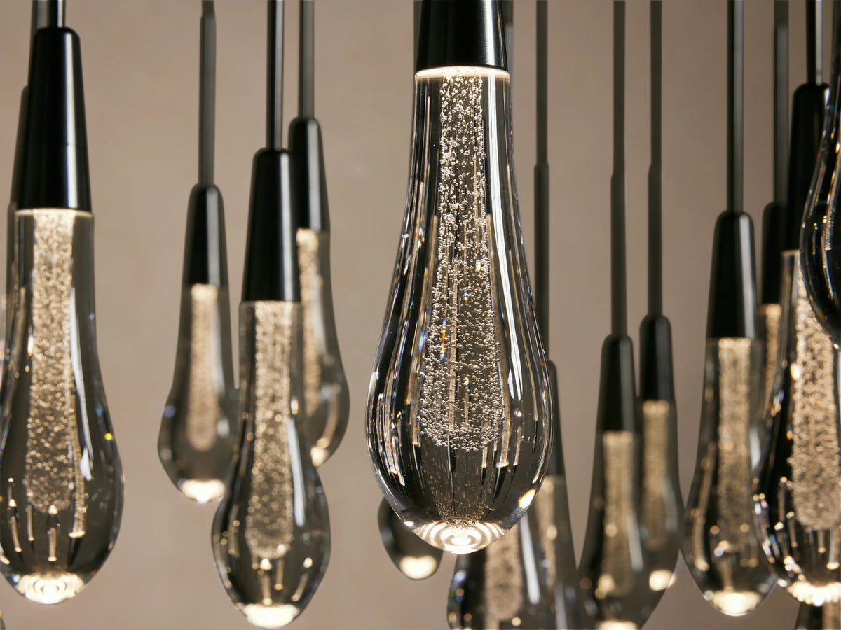 Close-up of several Soltaire Round Chandelier lights, featuring teardrop-shaped glass bulbs with cascading bubbles inside, suspended from black rods.