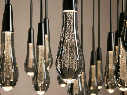 Close-up of several Soltaire Round Chandelier lights, featuring teardrop-shaped glass bulbs with cascading bubbles inside, suspended from black rods.