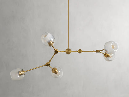 Brass chandelier with five arms, matte finish, globe-shaped glass shades, minimalist design, suspended from a central rod.