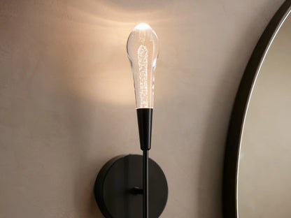 Double sconce with black round backplate, vertically aligned clear glass rods extending above and below on a beige wall.