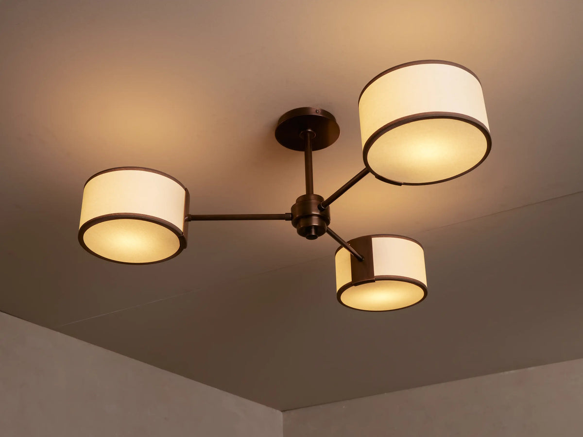 Close-up of a bronze Daphne Fabric Flush Mount with a cream fabric cylindrical shade and dark trim, emitting a warm glow.