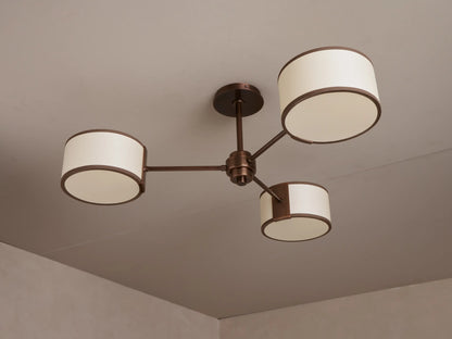Daphne Fabric Flush Mount: Bronze 3-arm ceiling light with three lit cylindrical cream fabric shades.