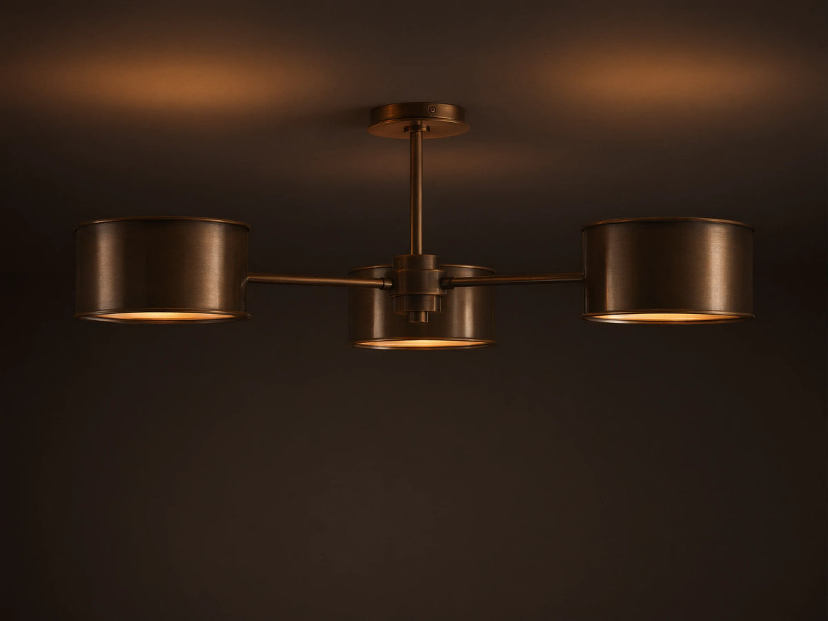 Daphne Metal Flush Mount in warm bronze with three cylindrical shades casting a soft, warm glow on a light ceiling.