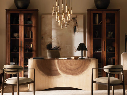 Soltaire Chandelier with many lit teardrop-shaped clear glass pendants, each with a brass cap, hanging at various lengths.