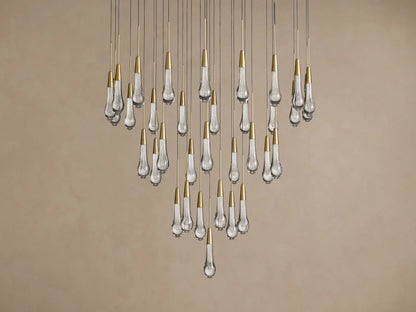 Soltaire Round Chandelier: cascading clear glass bubble pendants with shiny brass caps against a light beige wall.