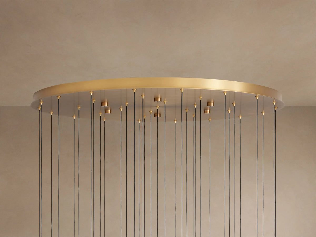 Soltaire Round Chandelier. Large brass-finished round plate with numerous thin black cords hanging down from golden fittings.