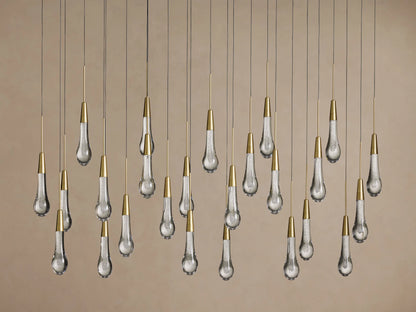 Soltaire Linear Chandelier: Many clear, teardrop-shaped glass pendants with internal bubbles & brass caps, hanging.
