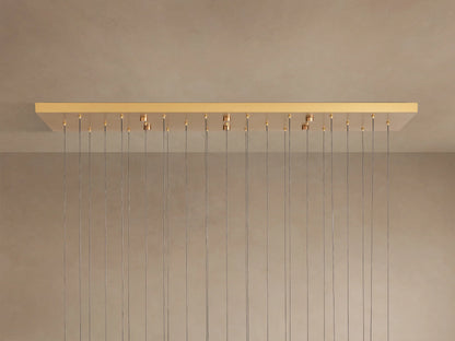 Soltaire Linear Chandelier with a rectangular brass-finished canopy mounted on a light ceiling, from which many thin wires hang.
