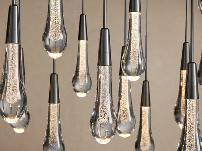 Close-up of Soltaire Round Chandelier with multiple teardrop clear glass pendants, dark metal tops, glowing LED bubbles inside.