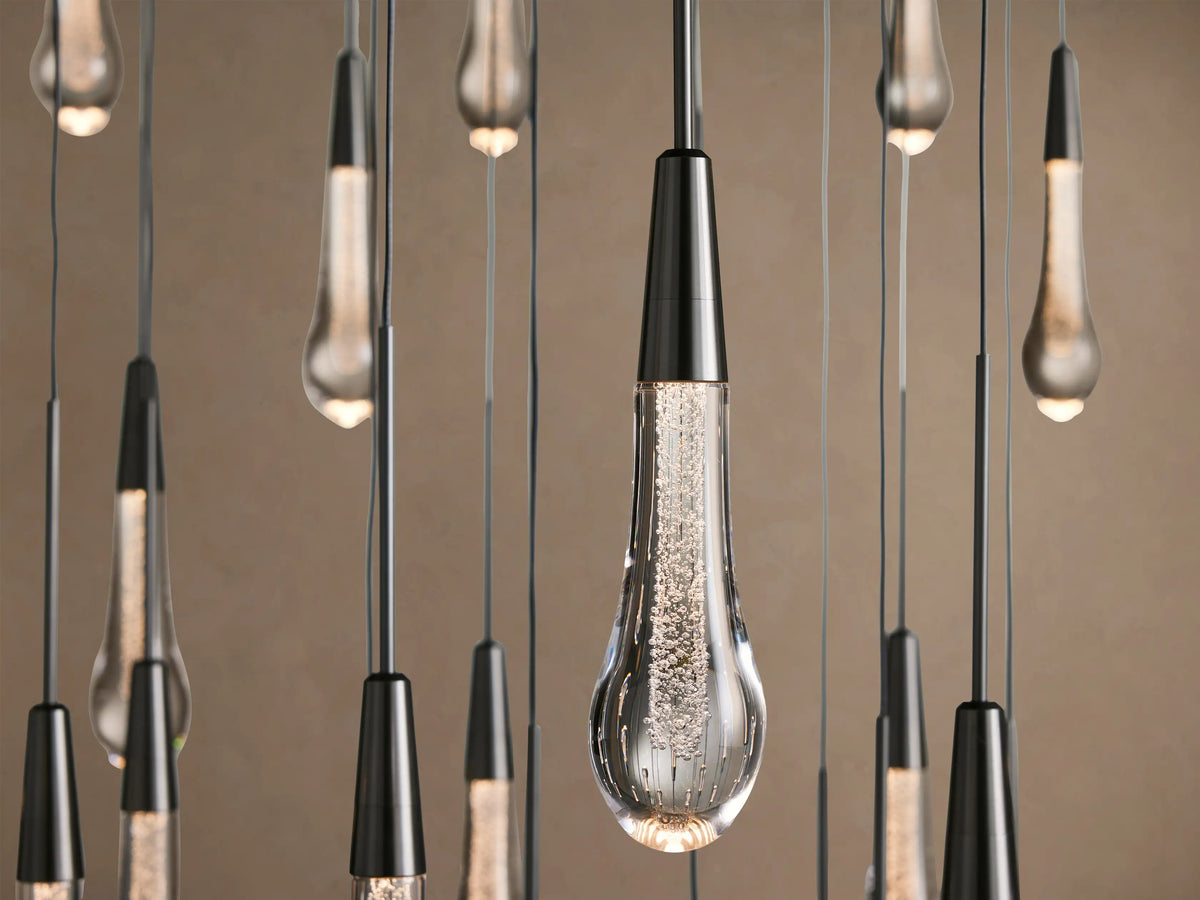 Soltaire Round Chandelier: numerous clear glass teardrop pendants, dark caps, hanging at staggered heights on a light wall.