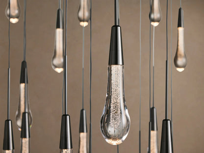 Soltaire Round Chandelier: numerous clear glass teardrop pendants, dark caps, hanging at staggered heights on a light wall.