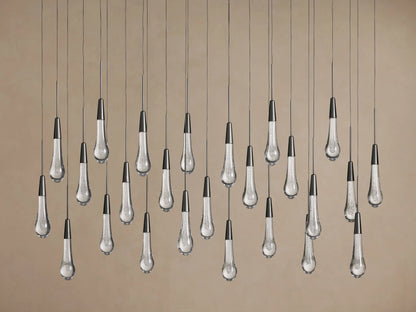 Soltaire Linear Chandelier: Many clear glass teardrop pendants with bubbles & dark metal tops hang against a beige wall.