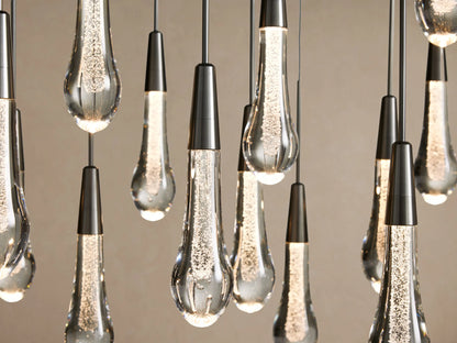 Soltaire Linear Chandelier: Many glowing clear glass teardrop pendants with internal bubbles, suspended from dark metal caps.