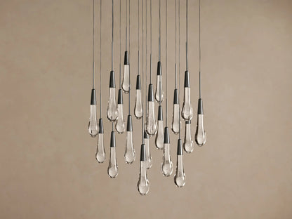 Soltaire Round Chandelier with multiple clear glass teardrop pendants, dark conical tops, hanging against a light brown wall.