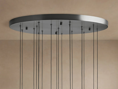 Soltaire Round Chandelier ceiling plate in brushed metal finish with many thin black cords hanging down against a beige ceiling.