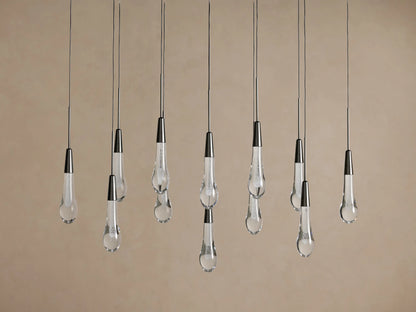 Soltaire Linear Chandelier with multiple clear glass teardrop pendants suspended at various heights from dark metal fixtures.