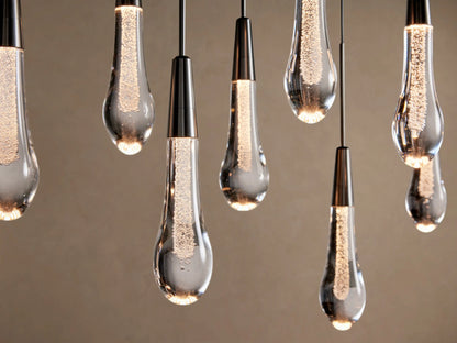Soltaire Linear Chandelier: illuminated clear glass teardrop pendants with sparkling internal bubbles & dark caps, hanging.