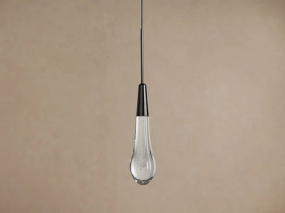 Soltaire Pendant, hanging vertically, with a dark nickel cap and a clear, bubble-filled teardrop glass shade glowing warmly.