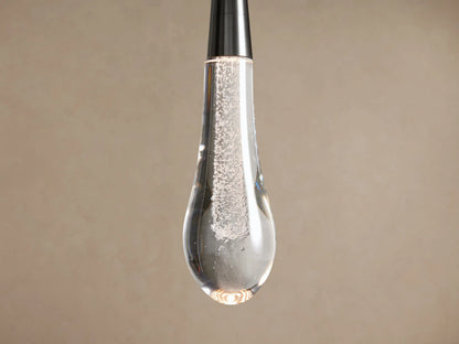 Nickel Soltaire Pendant with a clear, bubbly teardrop glass shade, hanging vertically against a light brown wall.