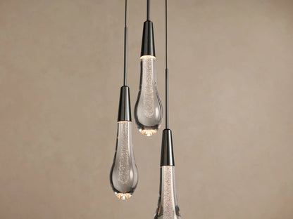 Three Soltaire Cluster Pendants with dark caps & clear, bubble-filled tear-drop glass shades, hanging against a beige wall.