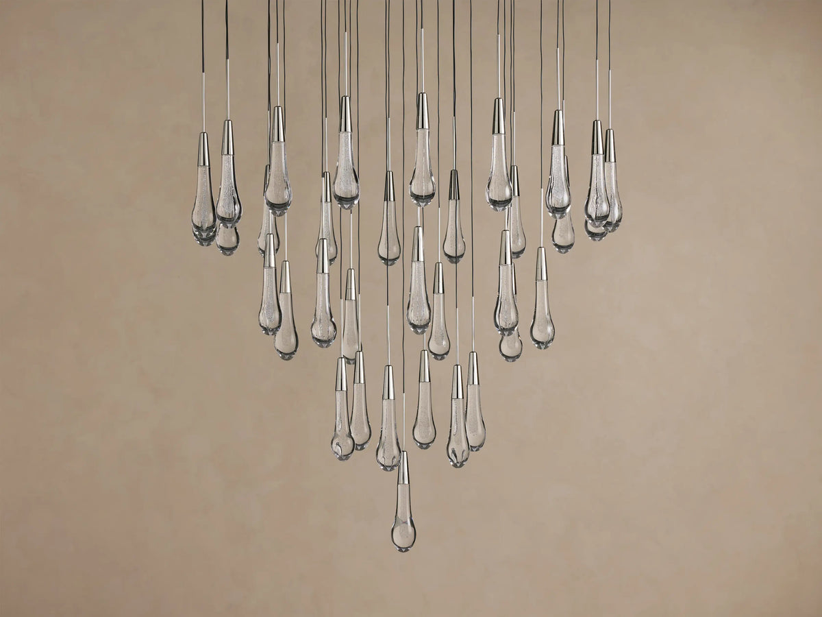 Soltaire Round Chandelier with cascading clear, textured glass teardrop lights with metallic caps, glowing.