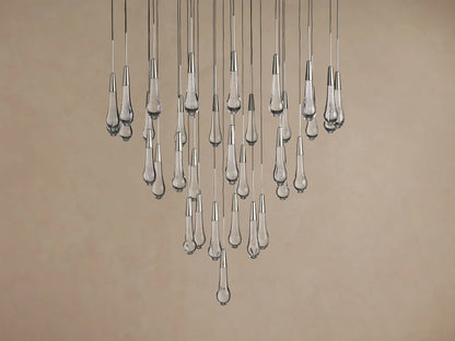 Soltaire Round Chandelier with cascading clear, textured glass teardrop lights with metallic caps, glowing.