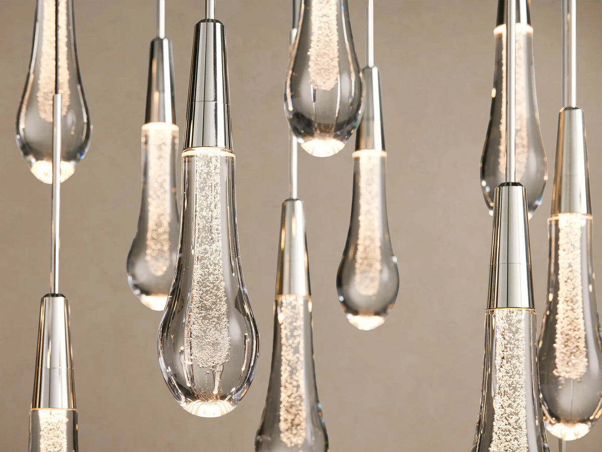 Soltaire Round Chandelier with many clear, sparkling teardrop glass pendants with nickel tops, hanging in a V-shape.