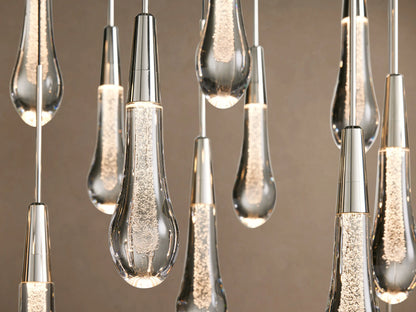 Soltaire Linear Chandelier: Many clear, textured teardrop glass pendants with silver caps hanging on black wires against beige.