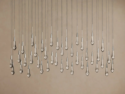 Soltaire Linear Chandelier: clear, textured teardrop glass pendants with silver tops hang illuminated at varying heights on a neutral background.